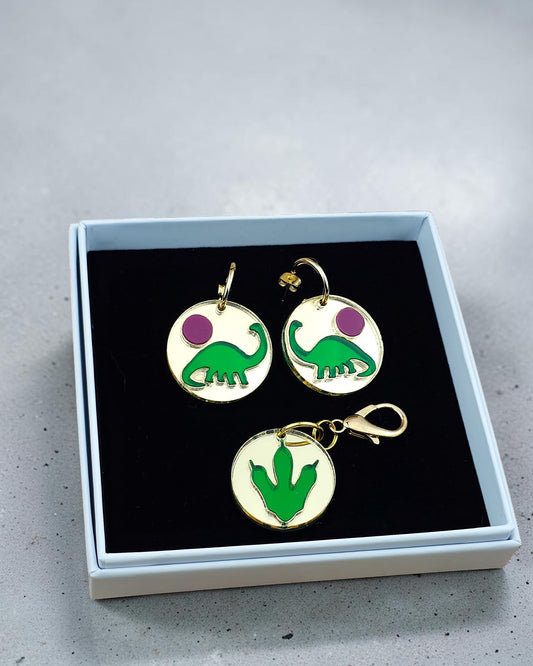 Morti's Fun Club Tiny Dino earrings featuring green dinosaurs and purple moons on gold-plated hoops in a gift box.