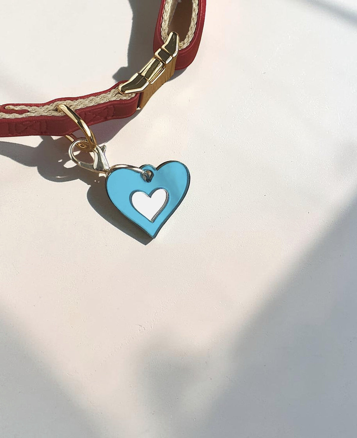 Morti's Fun Club light blue heart-shaped acrylic dog collar charm with a silver lobster clip on a red collar.