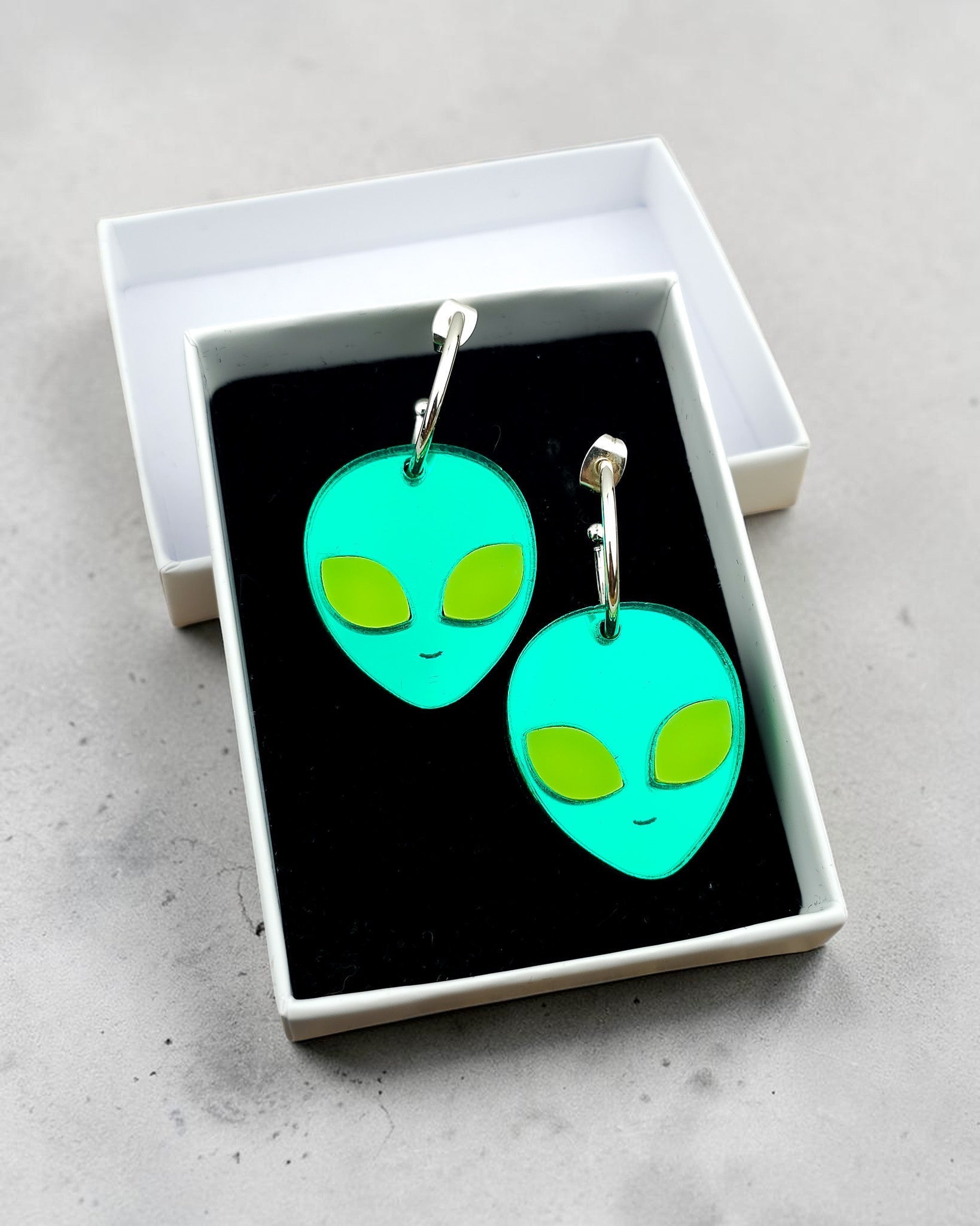 Morti's Fun Club alien face hoop earrings in cosmic mirror acrylic with fluorescent lime eyes in a gift box.