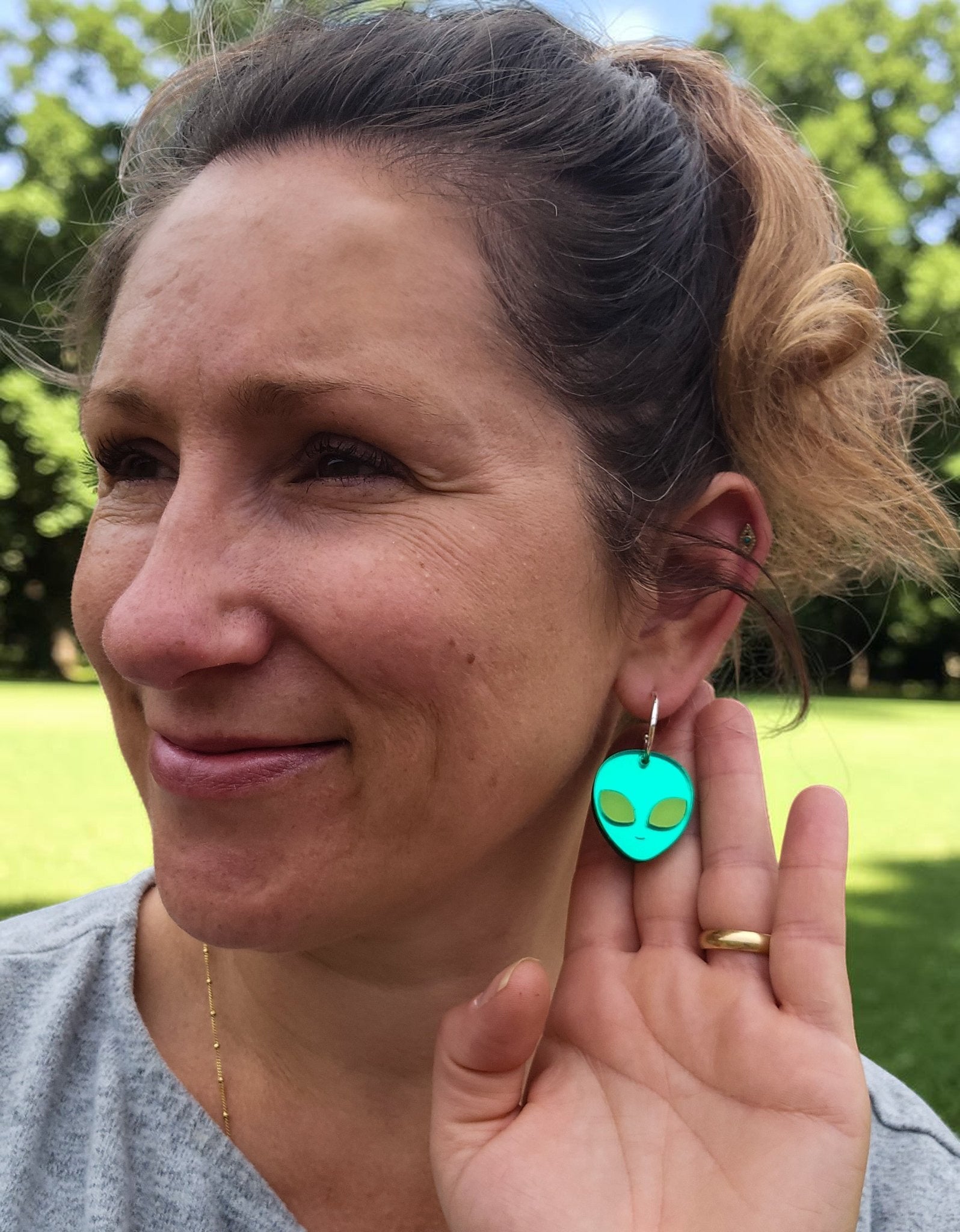 Morti's Fun Club alien face earrings in cosmic mirror acrylic with lime fluorescent eyes worn by a woman outdoors