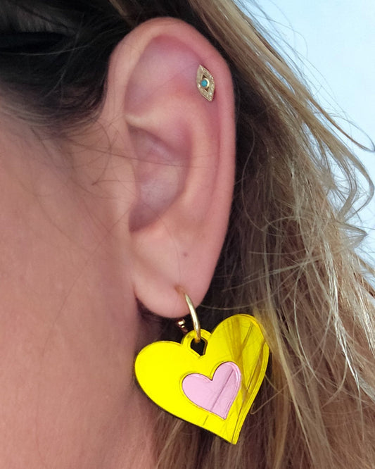 Morti's Fun Club Candy Canary heart earrings in yellow and pink mirrored acrylic on a gold hoop worn on an ear.