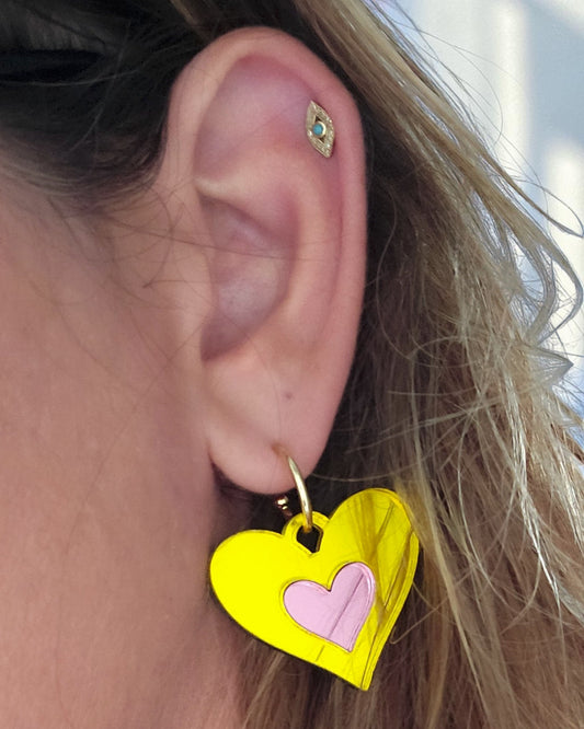 Morti's Fun Club Candy Canary heart earrings in yellow and pink mirrored acrylic on a gold hoop worn on an ear.