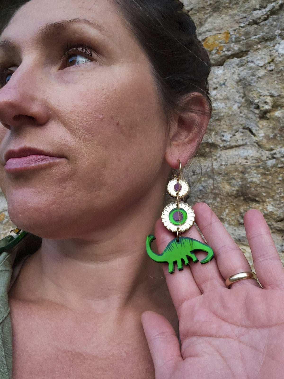 Morti's Fun Club gold-plated hoop earrings featuring green dinosaur and purple floral motifs worn by a woman