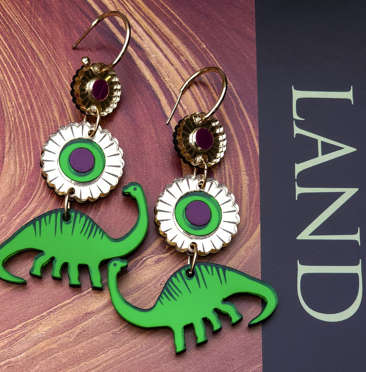 Morti's Fun Club Dino Royalty statement earrings featuring green dinosaur charms and gold-mirrored floral accents.