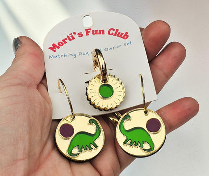 Morti's Fun Club gold-mirrored acrylic earrings and matching dog collar charm featuring green dinosaurs and purple suns