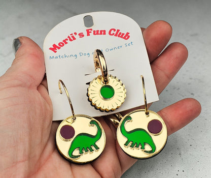 Morti's Fun Club gold-mirrored acrylic earrings and matching dog collar charm featuring green dinosaurs and purple suns
