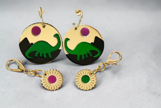 Morti's Fun Club Jurassic Moonrise earrings featuring a green dinosaur silhouette on a gold and black acrylic disc.