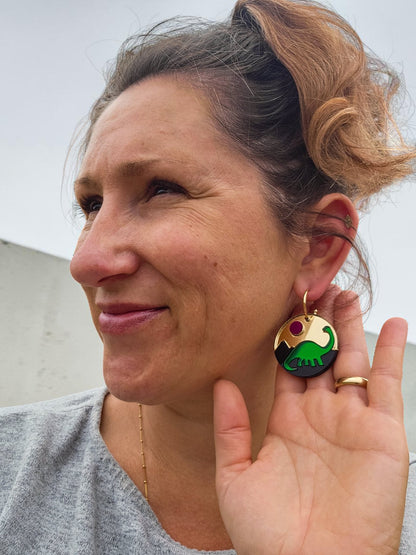 Morti's Fun Club Jurassic Moonrise circular earrings featuring a green dinosaur and pink sun on black acrylic