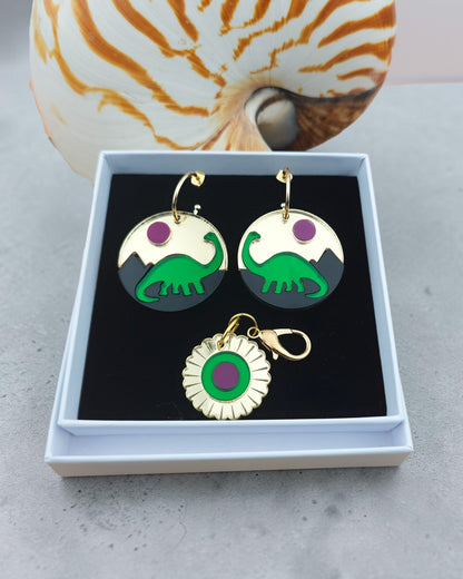 Morti's Fun Club Jurassic Moonrise earrings and matching charm featuring layered green dinosaur and pink sun design.
