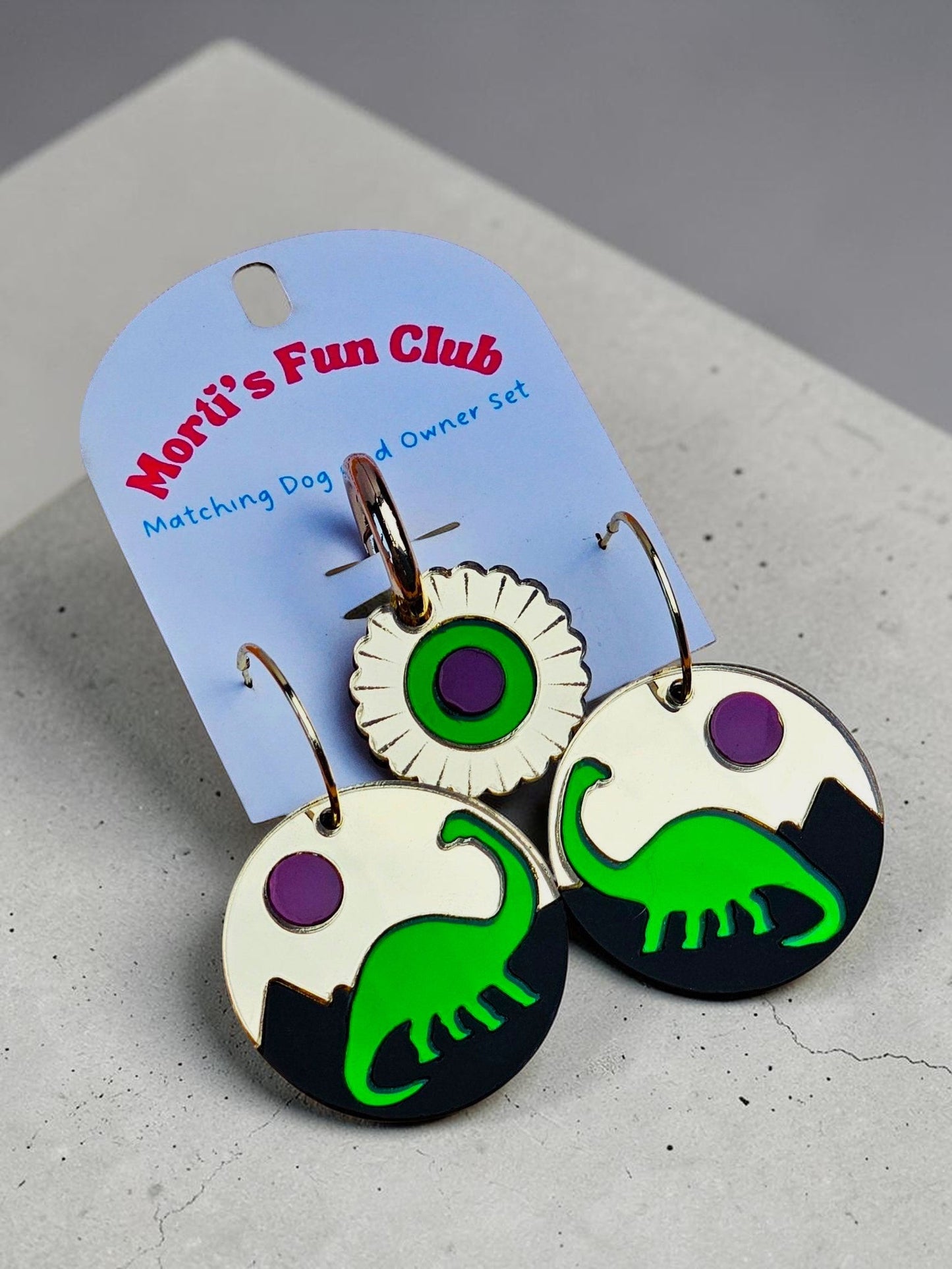 Morti's Fun Club Jurassic Moonrise twinning set featuring green dinosaur acrylic earrings and a matching collar charm.