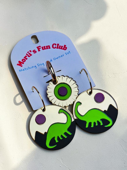 Morti's Fun Club Jurassic Moonrise twinning set featuring green dinosaur acrylic earrings and a matching collar charm.