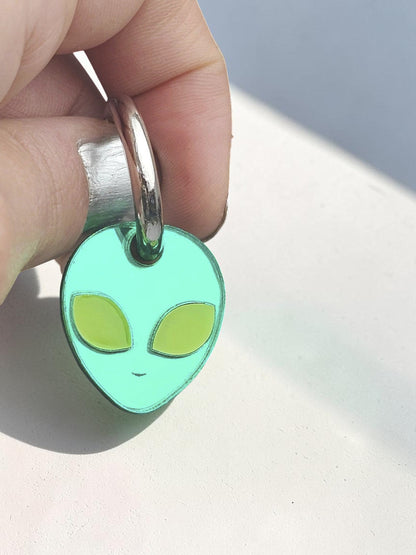 Morti's Fun Club green acrylic alien charm on a silver hoop earring against a dark celestial background