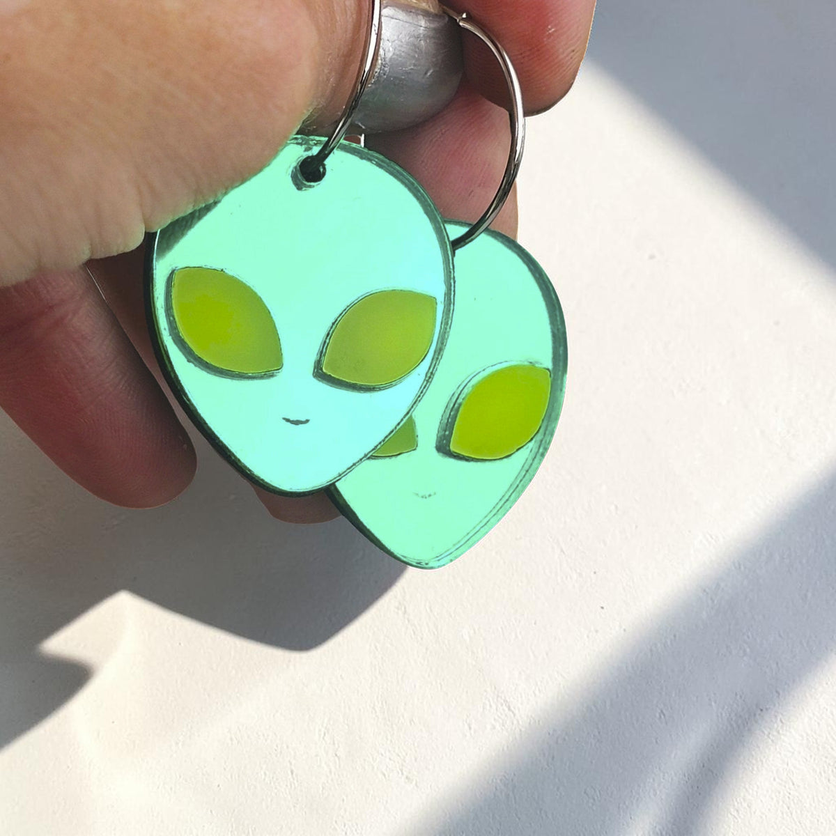 Morti's Fun Club green mirrored alien hoop earrings with yellow eyes held against a lunar space background