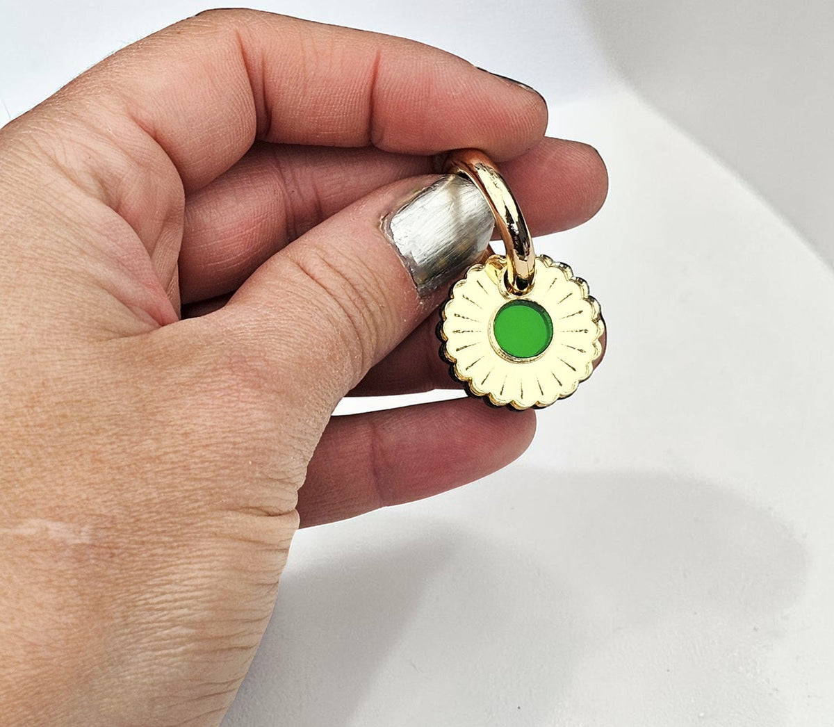 Morti's Fun Club gold-plated collar charm with a green inlaid acrylic center held in a hand