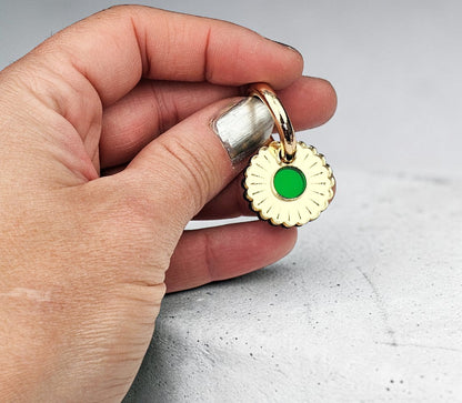Morti's Fun Club gold-plated collar charm with a green inlaid acrylic center held in a hand