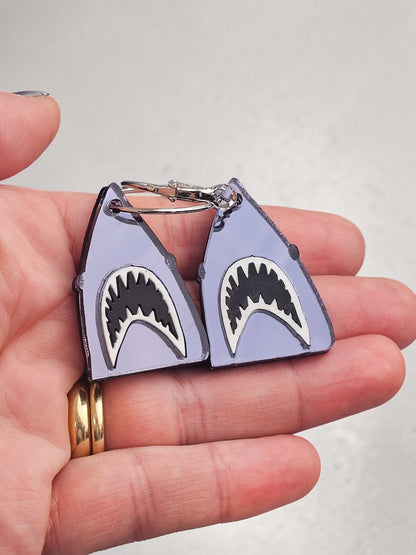 Morti's Fun Club shark-shaped acrylic earrings with black and white detailing held in a hand