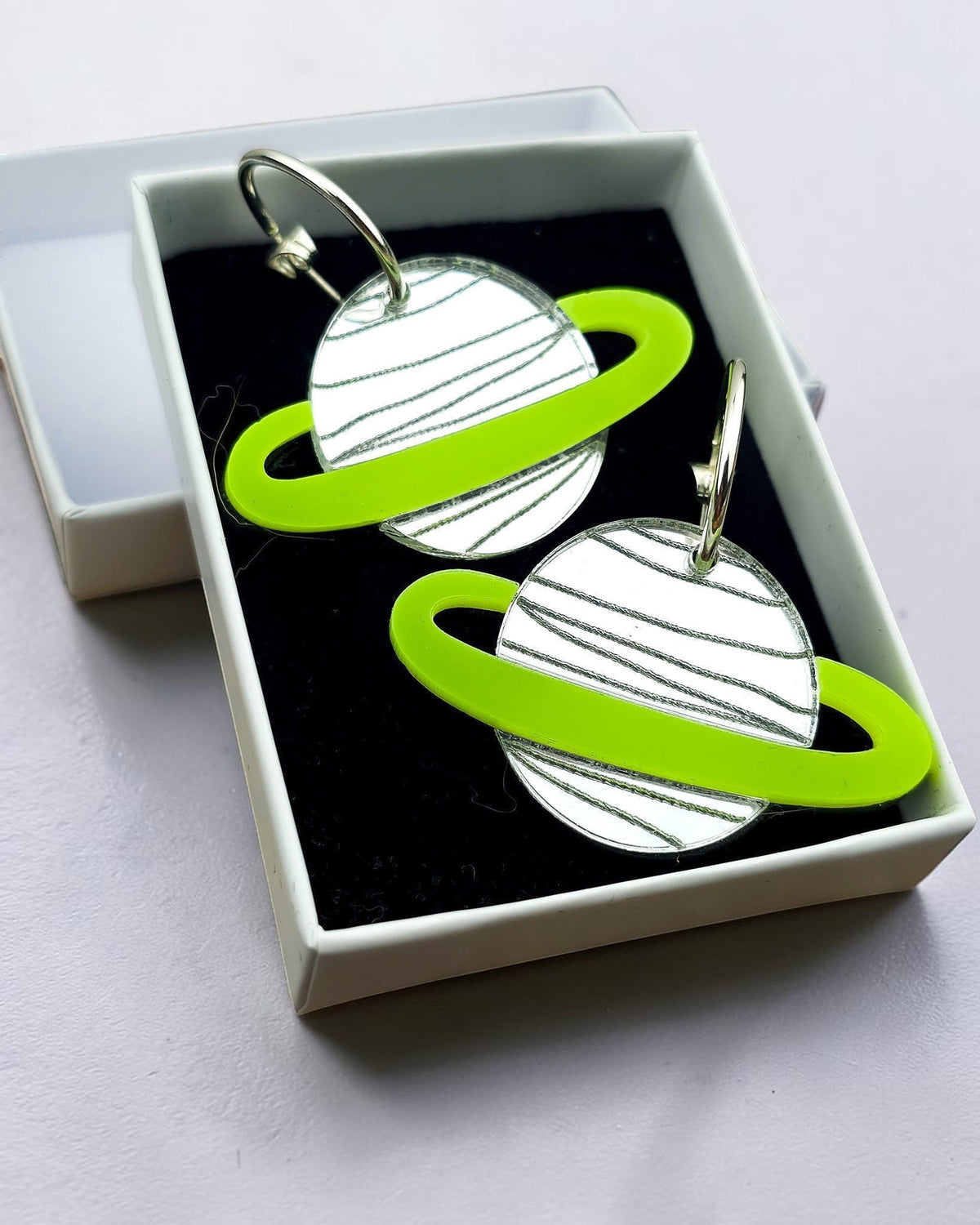 Morti's Fun Club Spacehopper Silver solar system earrings with mirrored silver planets and lime green rings in a box.
