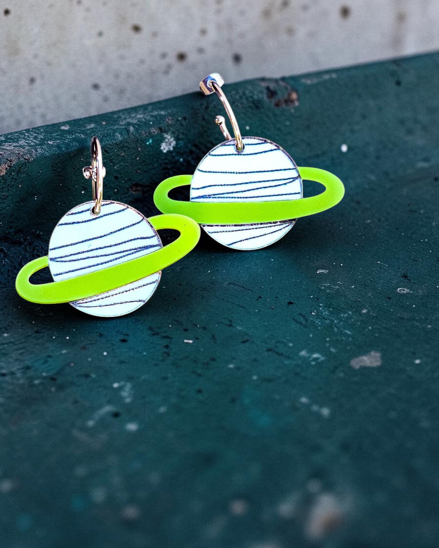 Morti's Fun Club silver planet earrings with lime green rings on gold-plated hoops against a pastel background