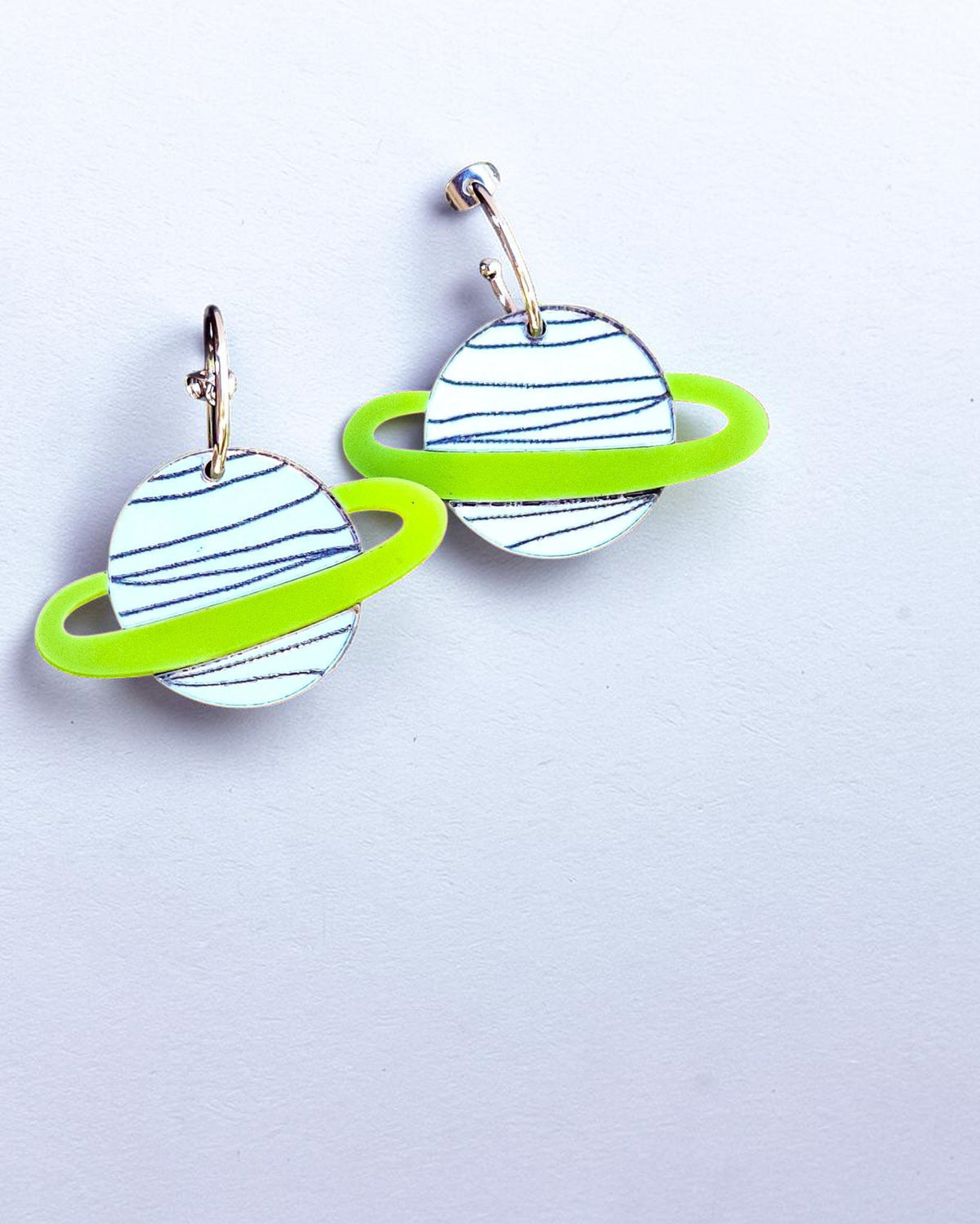 Morti's Fun Club silver planet earrings with lime green rings on gold-plated hoops against a pastel background