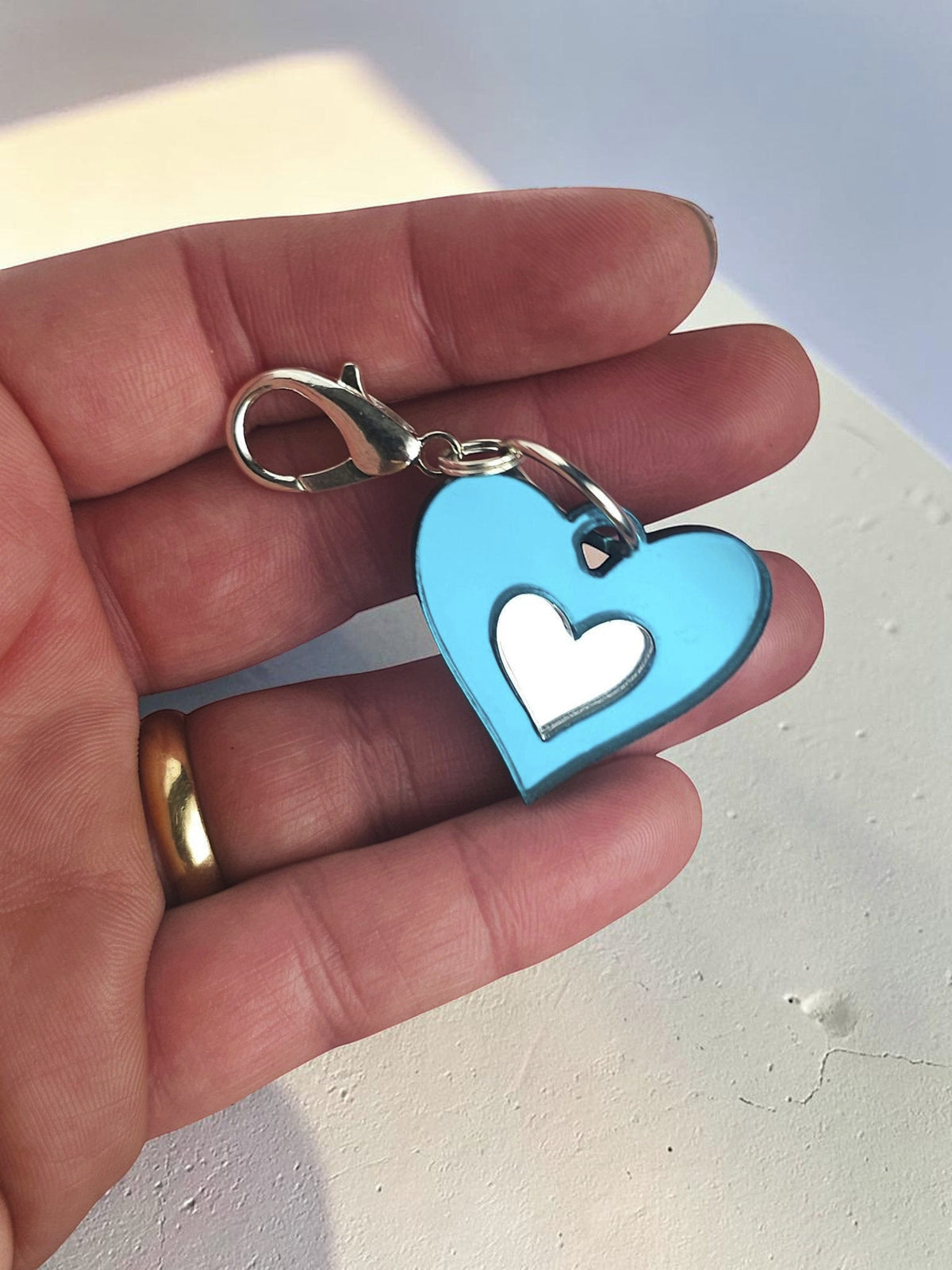 Morti's Fun Club Ice Queen heart dog collar charm in teal acrylic with a silver lobster clip held in a hand.