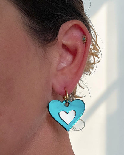 Morti's Fun Club Ice Queen heart earrings in teal and silver mirrored acrylic on a gold hoop worn on an earlobe.