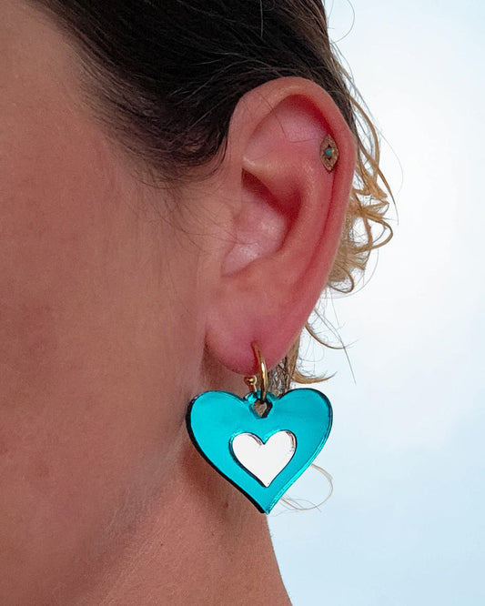 Morti's Fun Club Ice Queen heart earrings in teal and silver mirrored acrylic on a gold hoop worn on an earlobe.