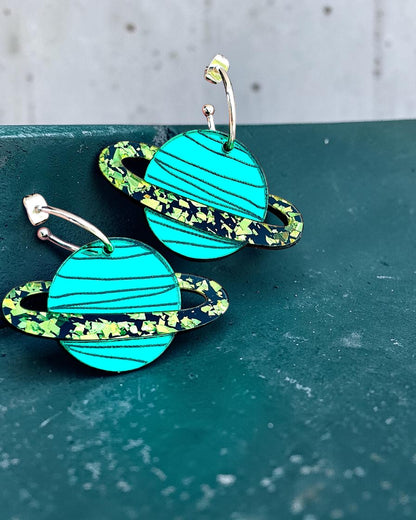 Morti's Fun Club teal mirrored acrylic planet earrings with lime glitter rings on gold-plated hoops.