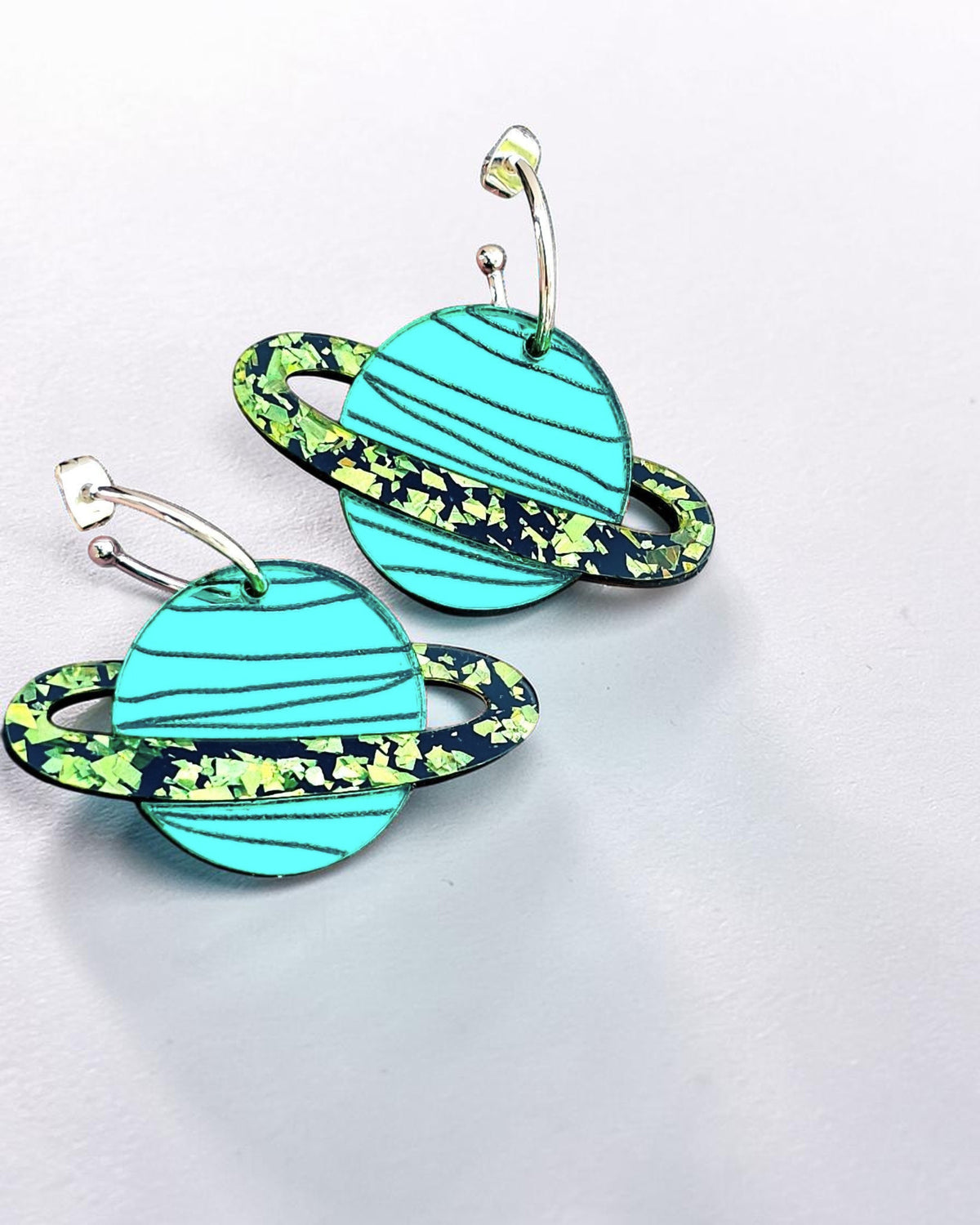 Morti's Fun Club teal mirrored acrylic planet earrings with lime glitter rings on gold-plated hoops.