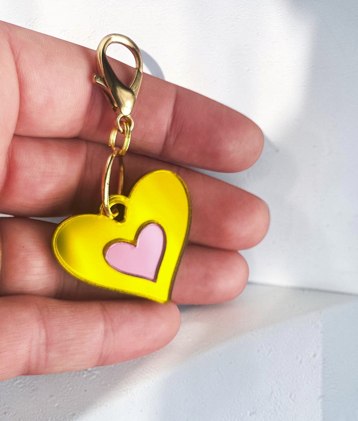 Morti's Fun Club Canary Candy heart-shaped acrylic dog collar charm in yellow and pink with a gold lobster clip